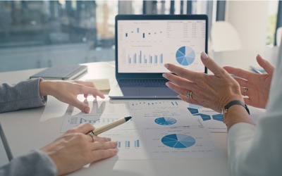 two people discussing investments with documents and laptop graphs